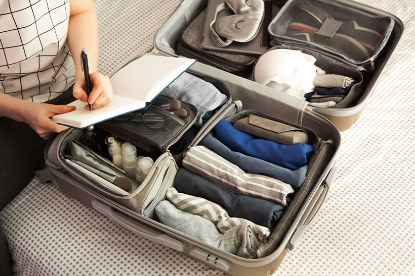 A Woman Is Taking Notes While Packing A Suitcase