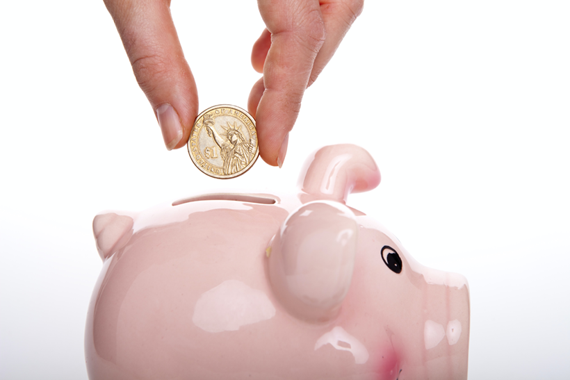 A Person Puts A Coin Into The Piggy Bank